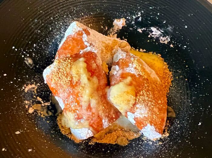 A trio of beignets dusted with powdered sugar and oozing with custard filling.