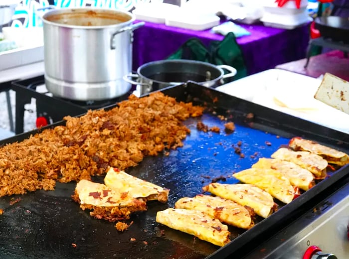 Tacos sizzling on an outdoor griddle, with a generous pile of chopped meat ready to be used as filling.