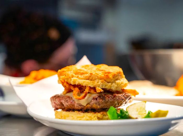 A burger nestled between two biscuit halves topped with fried onions.