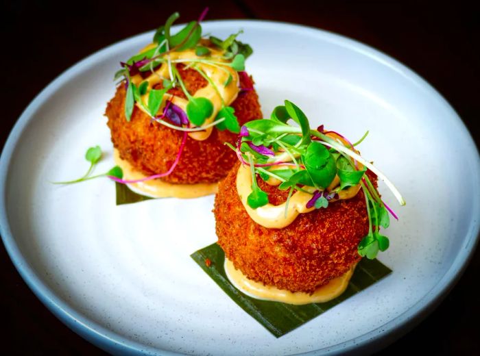 Two large croquettes resting on a bed of sauce, generously topped with additional sauce and garnished with herb sprigs.