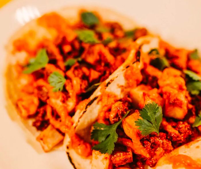 A close-up view of two tacos brimming with vibrant orange ingredients.