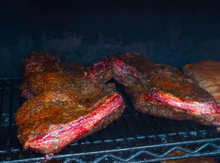 Two racks of ribs grilling on a barbecue.