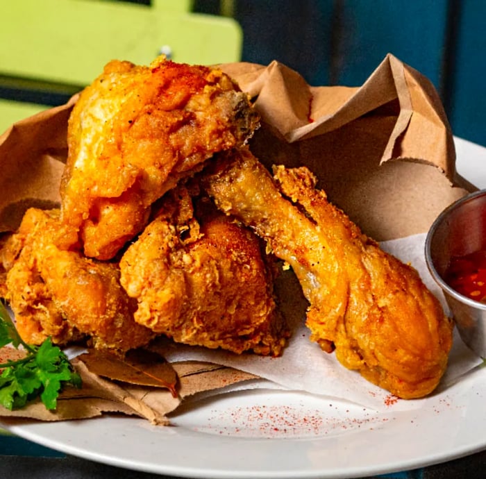 Crispy fried chicken pieces served on a plate alongside an open paper bag and dipping sauce.