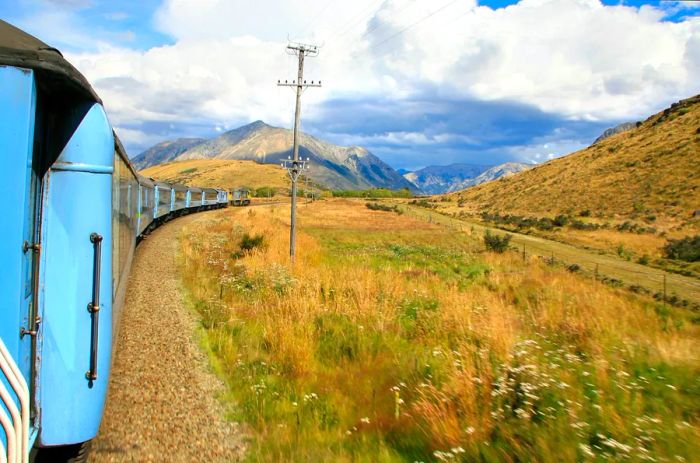 A blue carriage train winds its way through a mountainous area along the tracks