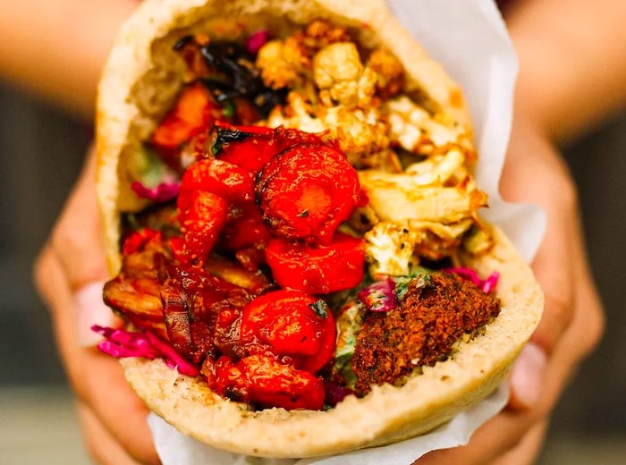 A close-up view of a pita sandwich brimming with roasted tomatoes, cauliflower, and falafel.