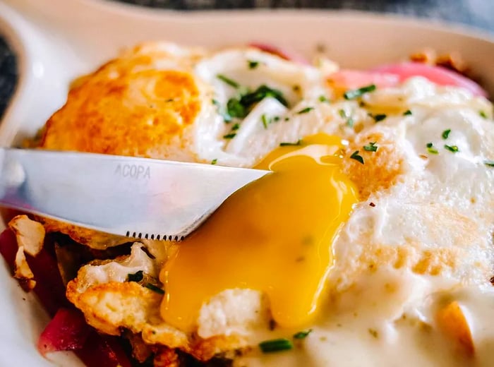 A knife cuts into a fried egg, spilling its rich yolk over a breakfast plate.