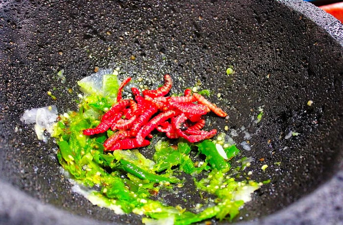 A heap of worms in a molcajete with crushed peppers.