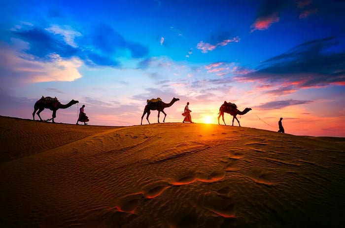 A camel safari traverses the Thar Desert at sunset in Jaisalmer, Rajasthan, India.