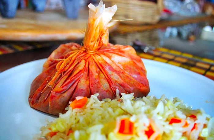 A small, bound red package of mixiote placed on a plate alongside a chopped salad.