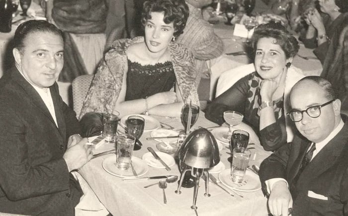 A vintage black and white image of four elegantly dressed individuals enjoying dinner at a restaurant.