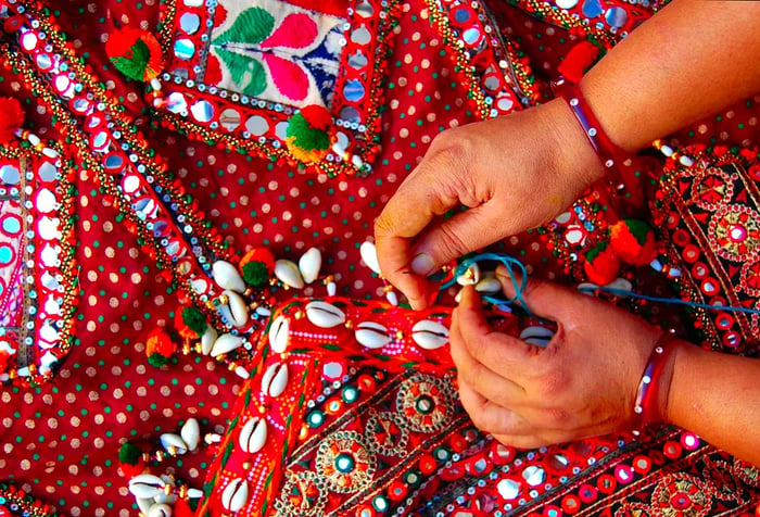 A woman stitches intricate patterns onto vibrant red fabric, a tradition from the Rann of Kachchh in Gujarat, India.