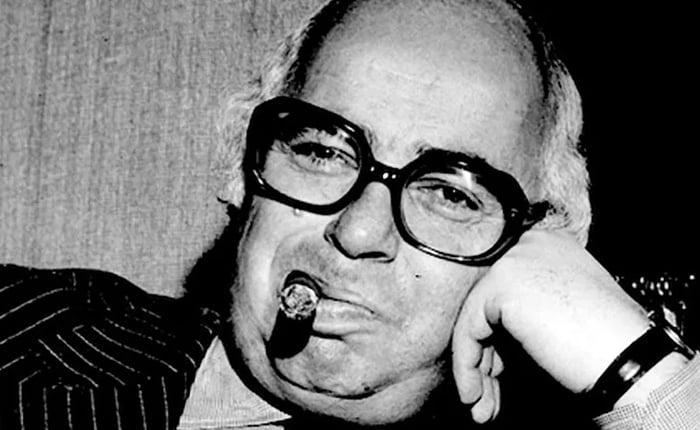 A black and white image capturing a man in thick-rimmed glasses, savoring a cigar.