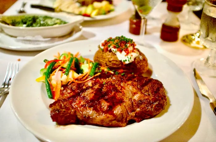 A sizable steak accompanied by a baked potato and a medley of vegetables.