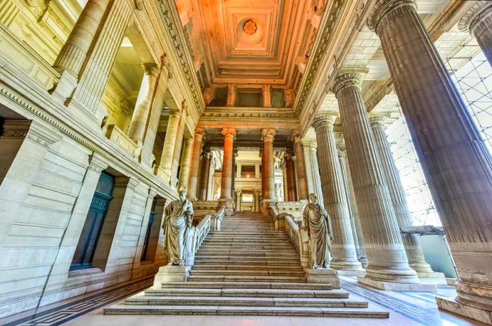 A grand marble staircase adorned with majestic neoclassical columns and statues inside the Palais de Justice, Brussels