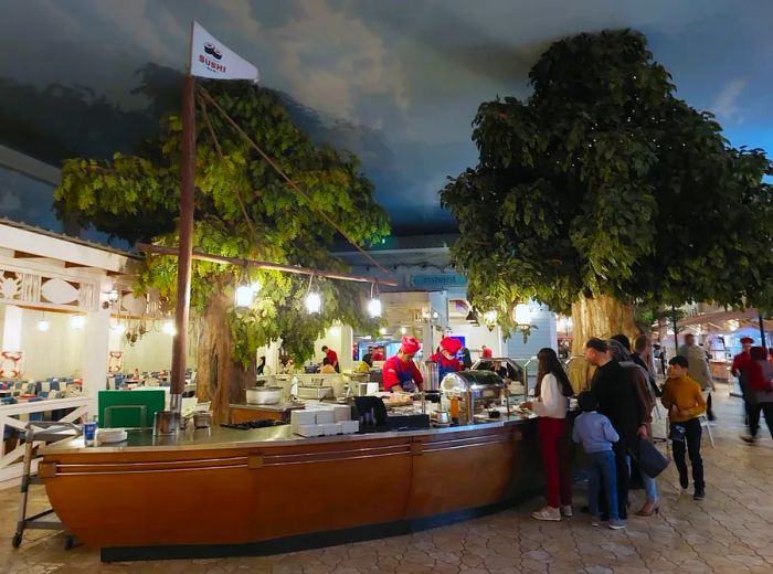 A sushi serving station designed like a boat, where customers line up for food on one side while chefs prepare dishes inside.