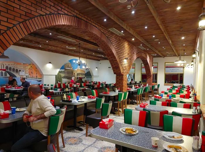 Diners are seated in chairs adorned with the colors of the Italian flag, surrounded by a dining room featuring exposed brick arches and murals depicting famous Roman landmarks.