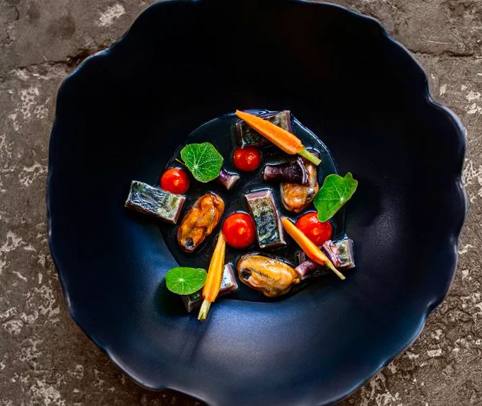 A deep, textured bowl filled with a mix of mussels, vegetables, and herbs.