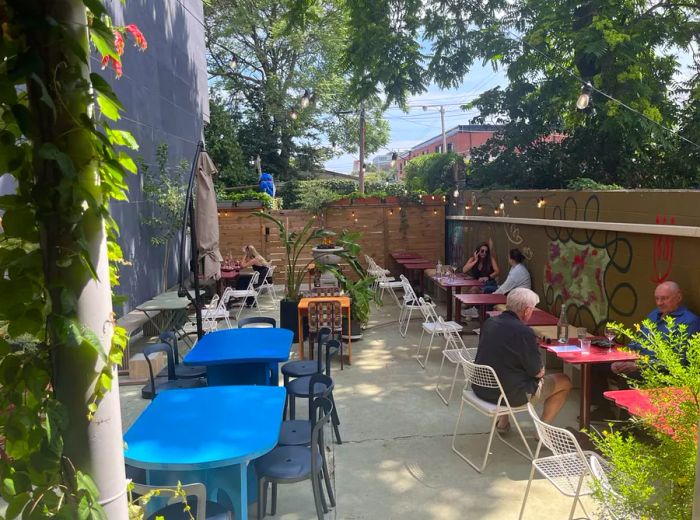 Patrons relax at small tables on an outdoor patio in the afternoon sunshine.