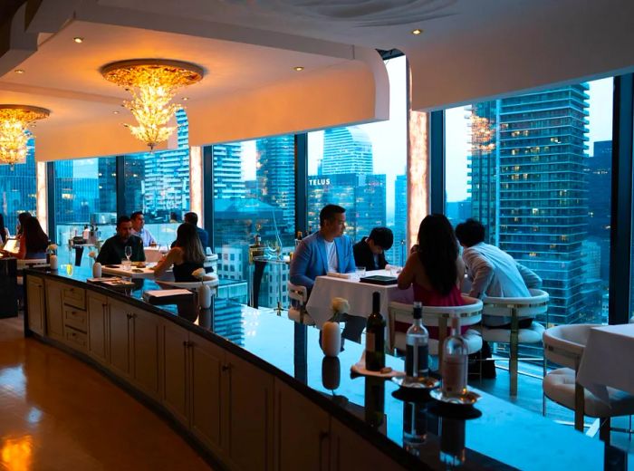 Diners enjoy a luxurious setting with expansive windows offering views of Toronto's skyline.