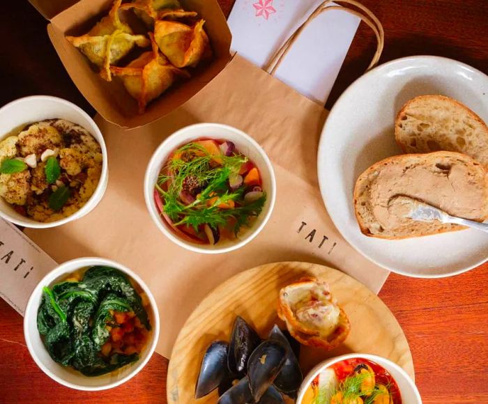 A wooden table adorned with a variety of dishes and paper bags branded with the Tati logo.