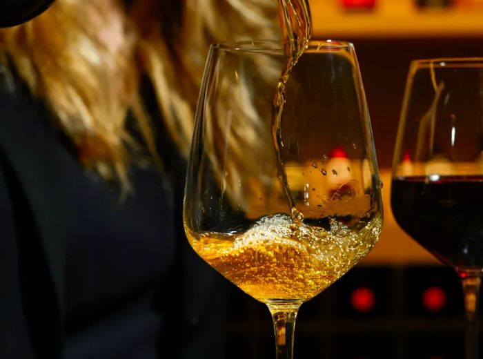 A person pours a glass of white wine into a wine glass.