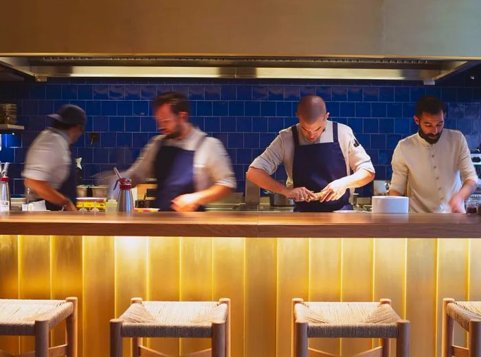 A kitchen counter featuring four team members diligently working behind it, with four empty stools lined up in front.