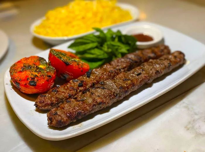 A platter featuring two long skewers of meat accompanied by fresh vegetables.