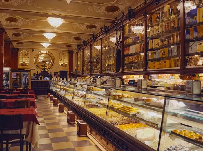 A lengthy pastry counter adorned with intricate carvings, complemented by tables set on a stylish checkerboard floor.