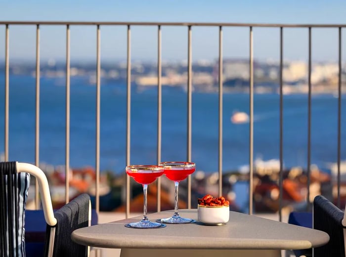 A small table holds cocktails and nuts beside two midcentury modern chairs, overlooking the river and the city below.