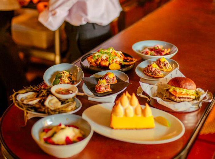 A selection of dishes displayed on a counter, featuring oysters, tartare, sandwiches, and a meringue-topped dessert.