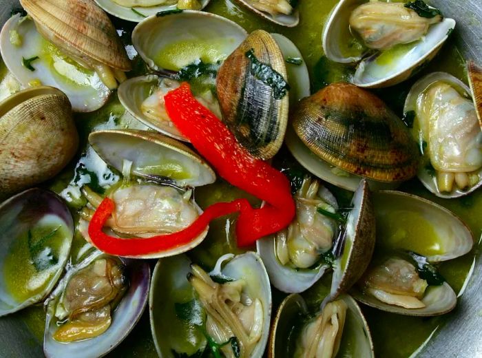 A serving of clams cooked in a flavorful broth, garnished with fresh vegetables.