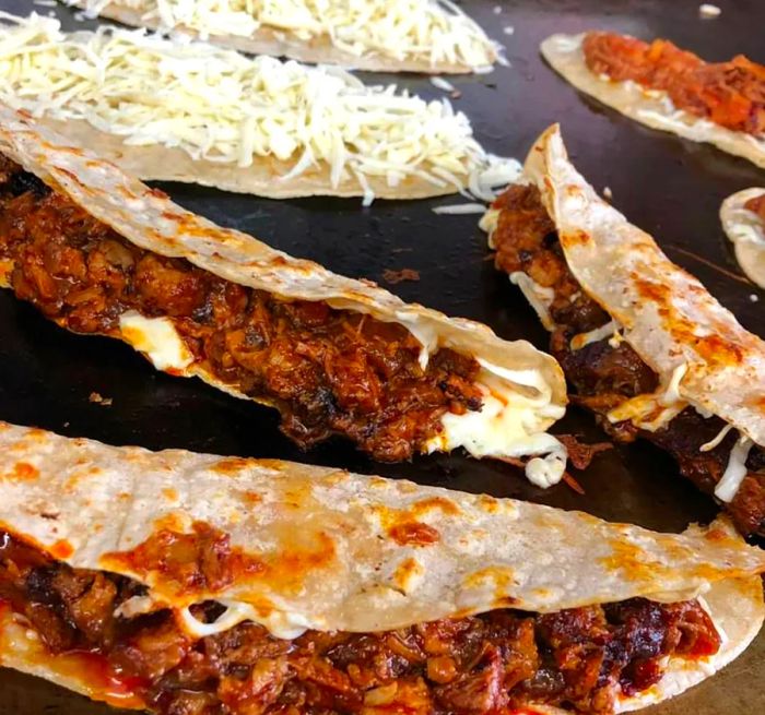 Quesadillas bursting with melted cheese on the griddle.