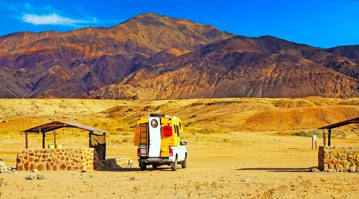 A camper van overlooks the orange desert with mountains in the background. Atacama, Chile