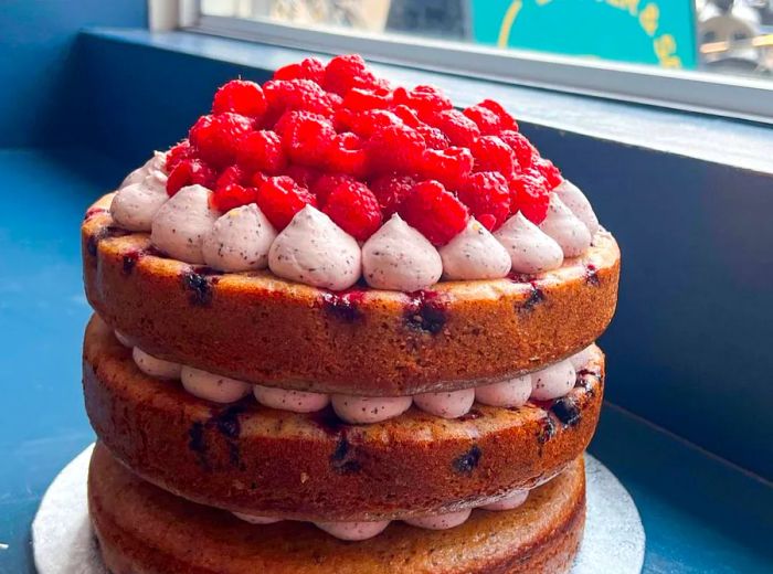 A three-layer cake adorned with icing and topped with fresh raspberries.