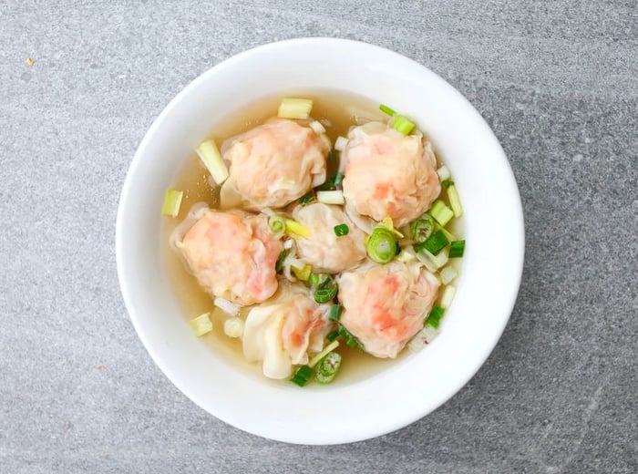 A bird's-eye view of a bowl of wontons swimming in soup, garnished with fresh herbs.