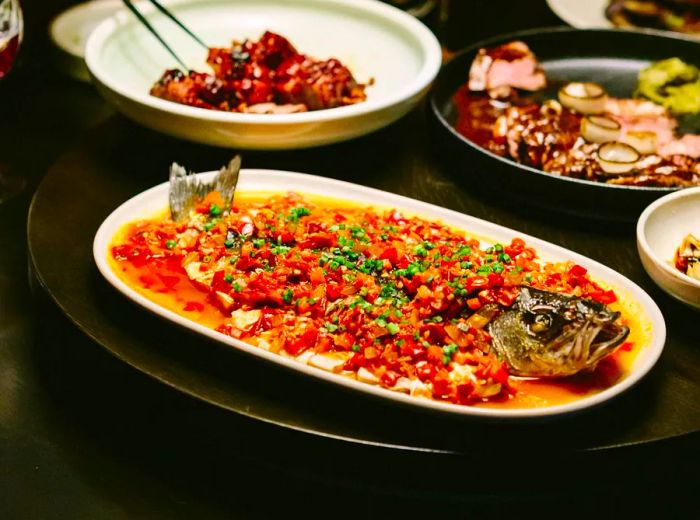 A whole fish adorned with diced spices, presented alongside its head and tail and an array of other dishes.