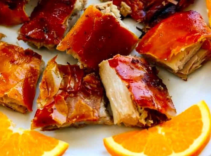 Tender chunks of roast pork adorned with crispy skin and garnished with orange slices.