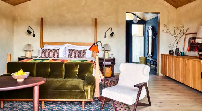 A vibrant hotel room featuring a plush green sofa, a four-poster bed, mid-century decor, and soaring ceilings.