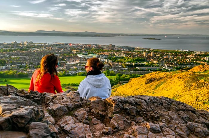 Girls lounging on the slopes of Arthur's Seat, gazing at Edinburgh