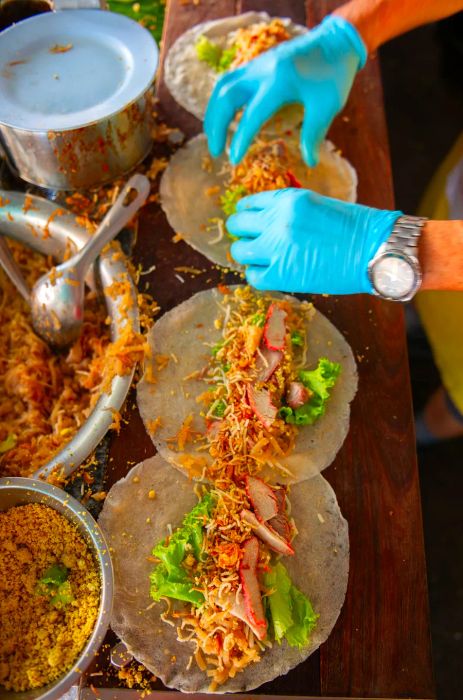 Hands clad in blue gloves prepare spring rolls.