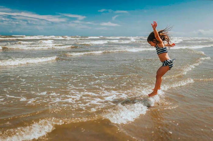 A young girl splashing joyfully in the water at a Texas beach.