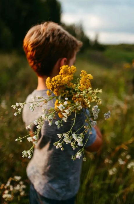 A child strolls through a field adorned with clusters of white and yellow wildflowers.