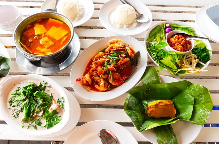 A variety of southern Thai and Phuket-style dishes beautifully arranged on a white-slat table.