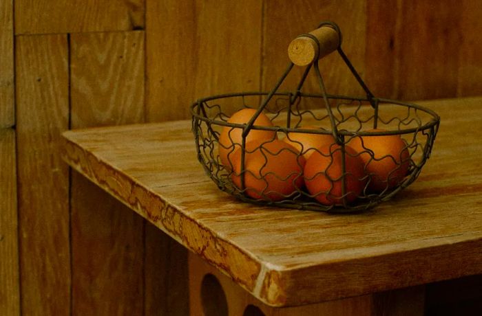 A wire basket filled with brown eggs sits atop a wooden table.