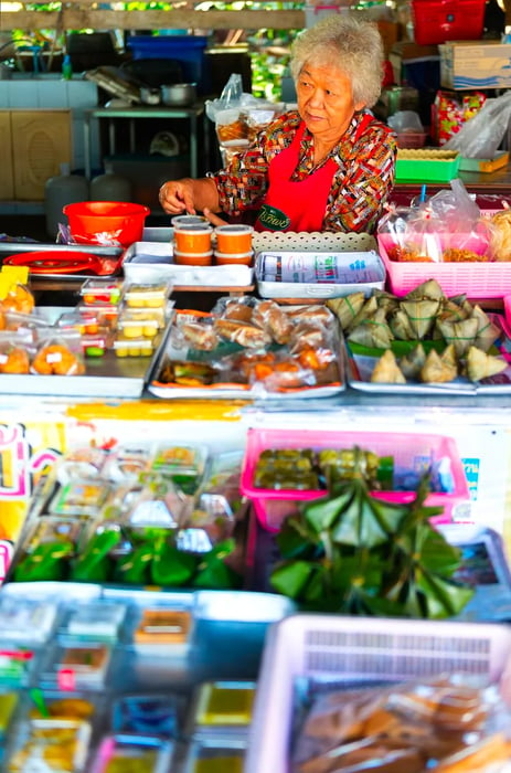 An elderly vendor glances skeptically behind a vast display of snacks.