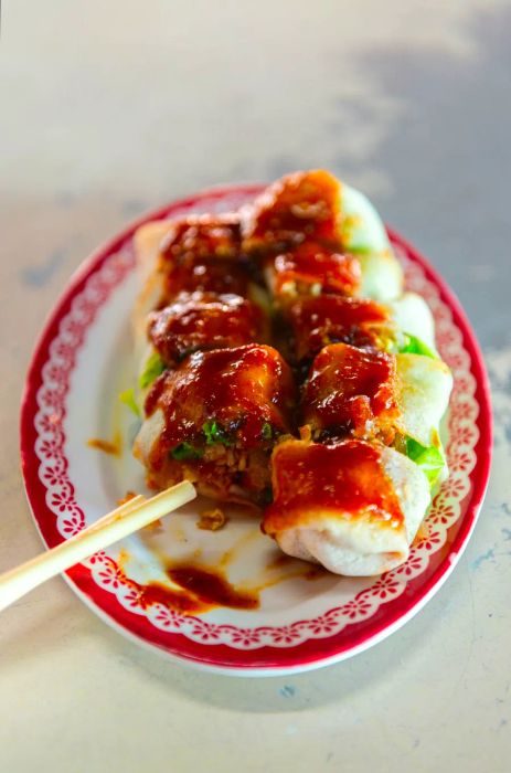 A spring roll, drizzled with sauce and sliced, with chopsticks resting nearby.