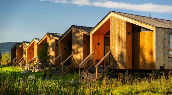 A collection of wooden cabins under a clear blue sky, surrounded by lush green grass.