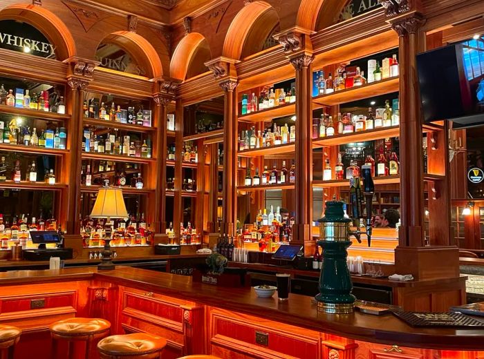 An interior of a bar featuring shelves stocked with liquor, framed by large, intricately carved wooden arches.