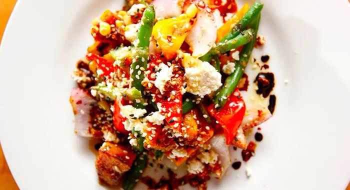 A close-up of a salad featuring roasted vegetables, crumbled cheese, and a variety of sauces.