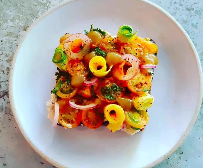 An overhead view of a square slice of toast adorned with various vegetable curls, presented on a white plate against a marble backdrop.